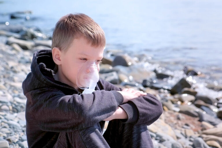 Portrait child boy uses nebulizer inhaler mask to treatment of asthma seaside.