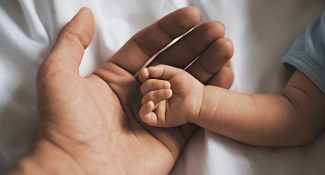 Close-up small hands of baby is lying in men of his father hands, concept of caring, fatherhood, family