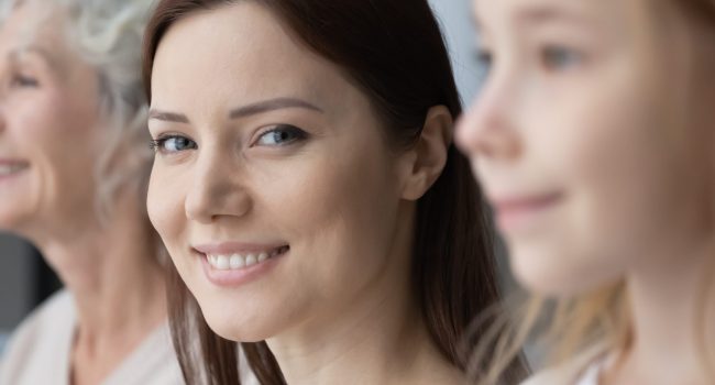 Wide image close up head shot smiling beautiful young woman looking at camera, posing with pretty little daughter and mature mother, free generations of women standing in row, growing process